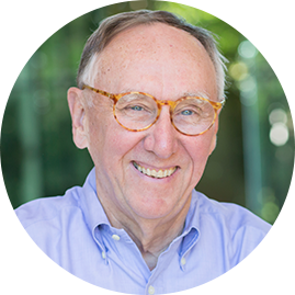 Esri President Jack Dangermond smiling wearing light brown round glasses and a blue shirt