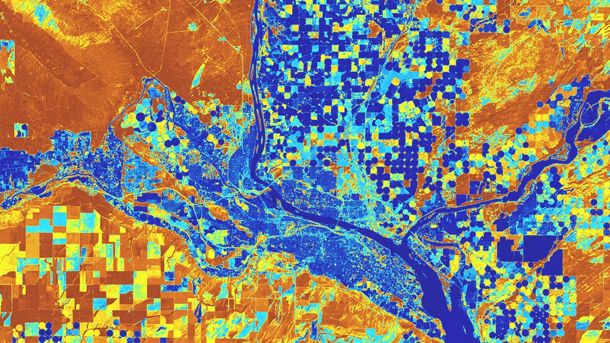 Ein Satellitenbild zeigt Grundstücke entlang eines Flusses mit quadratischen und kreisförmigen Feldern, die blau, orange und gelb markiert sind.