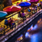 A small outdoor café seating area filled with chatting diners beside a peaceful lake reflecting swirling blue color